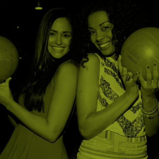 two women holding bowling balls and smiling