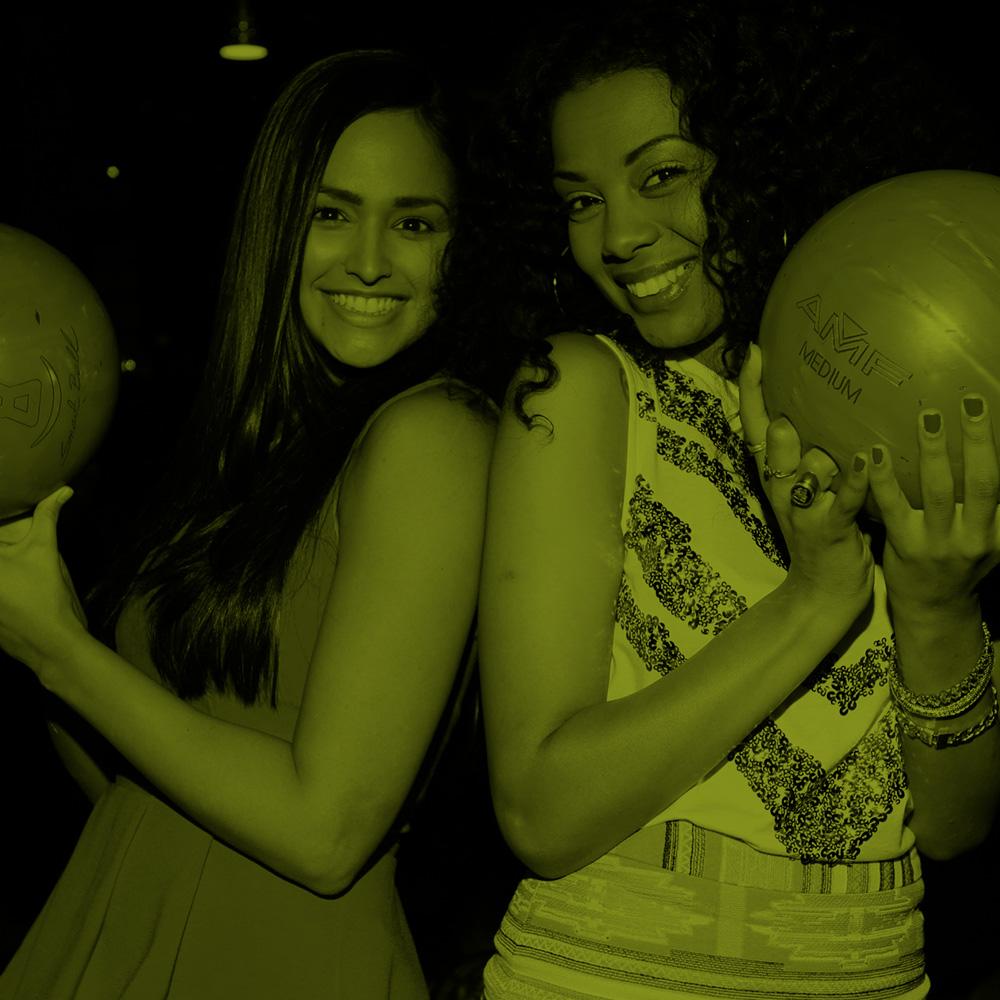 two women holding bowling balls and smiling